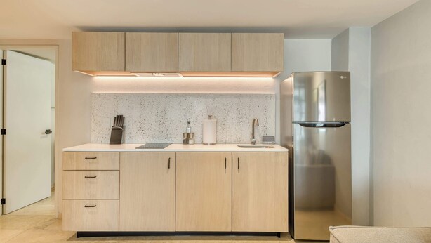 A modern kitchen with light wood cabinets, a stainless steel refrigerator, and a countertop with a sink and utensils. - Modern King Studio in Central Roma Norte (Ciudad de México)