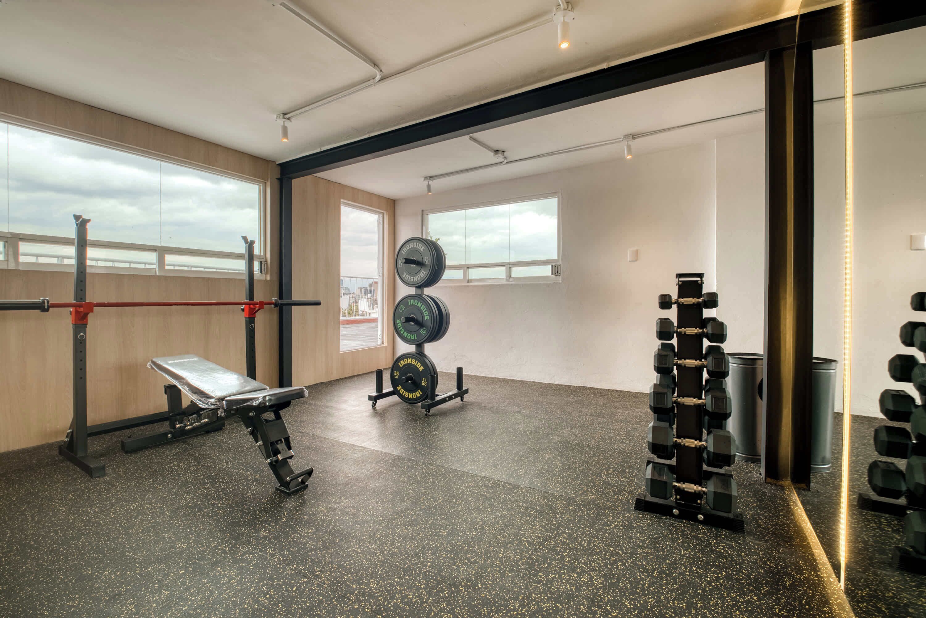 Une salle de sport équipée de matériel de musculation, d’un banc et de grandes fenêtres.