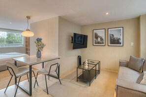 Ein modernes Wohnzimmer mit einer Couch, einem Esstisch mit Stühlen, einem an der Wand befestigten Fernseher und gerahmten Bildern.