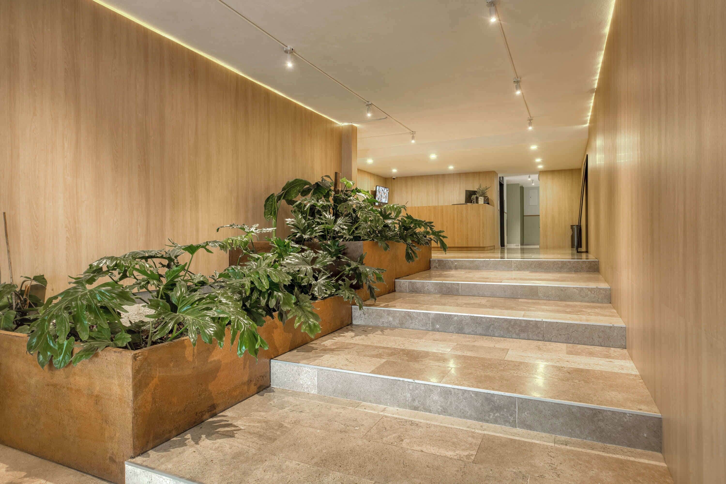 A modern hotel lobby with a wooden wall, a reception desk, and a staircase with potted plants.
