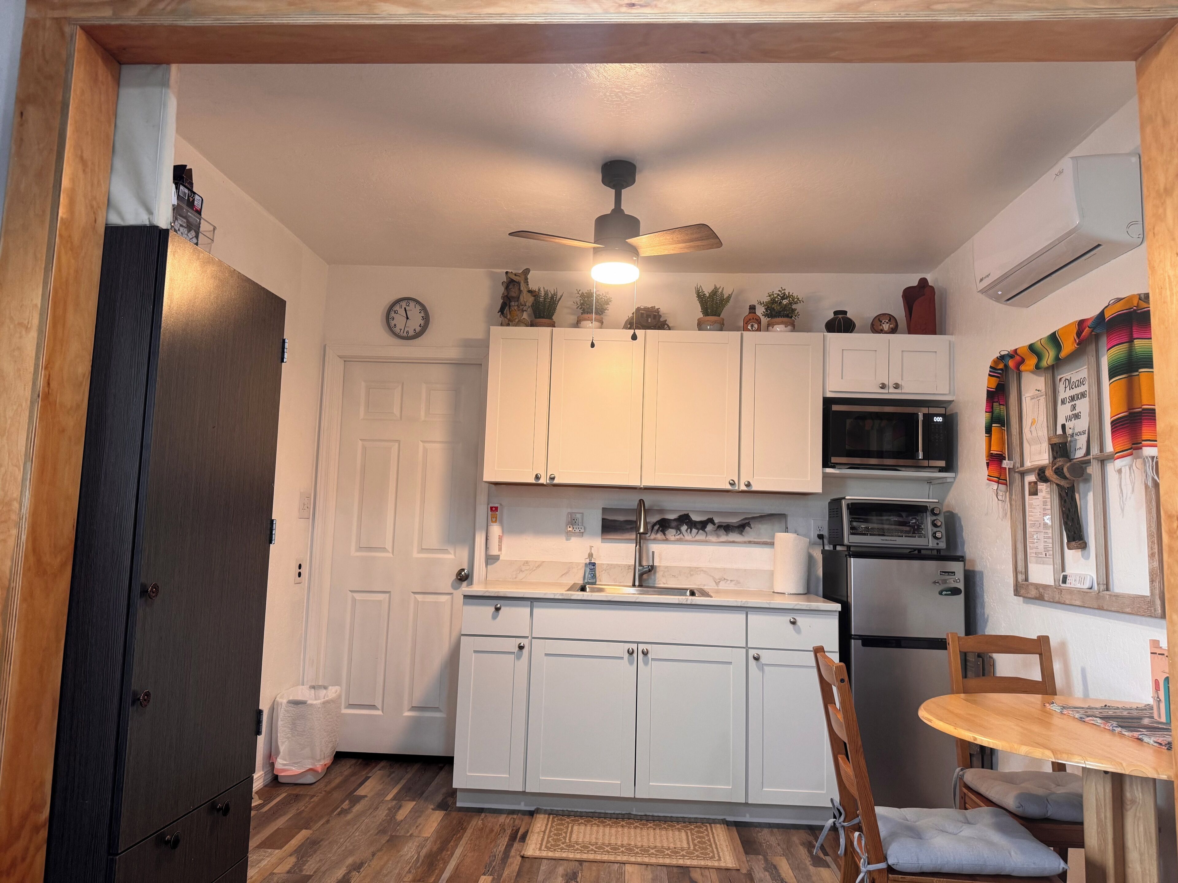 A compact kitchen with white cabinets, a microwave, an oven, and a ceiling fan.
