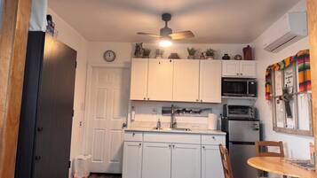 A compact kitchen with white cabinets, a microwave, an oven, and a ceiling fan.