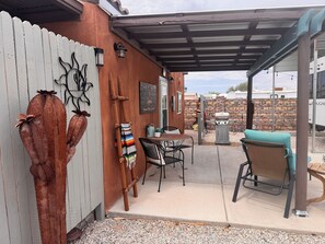 A covered patio area with a table and chairs, a barbecue grill, and decorative cacti. - A GREAT PRICE! FOR A COZY CASITA, SECURED ON A LARGE PRIVATE LOT ALL TO YOURSELF (Yuma)
