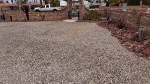 A gravel driveway leading to a gated entrance with a brick archway, surrounded by palm trees and a parked truck. - A GREAT PRICE! FOR A COZY CASITA, SECURED ON A LARGE PRIVATE LOT ALL TO YOURSELF (Yuma)