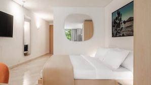 Quarto de hotel moderno com cama, espelho redondo, pintura e televisão.