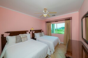 Ein Hotelzimmer mit zwei Betten, einem Deckenventilator, einem Fenster mit Vorhängen und Blick auf einen Golfplatz.