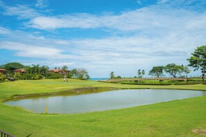 A golf course with a pond, palm trees, and a clear sky. - Del Mar 3C - 3 bdr 2 bath -  Ocean View (Playa Herradura)