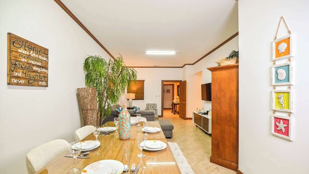 A dining area with a wooden table set for four, a large plant, and a wall with a decorative sign. - Veranda 1H -  3 bdr 3 bath Family (Playa Herradura)