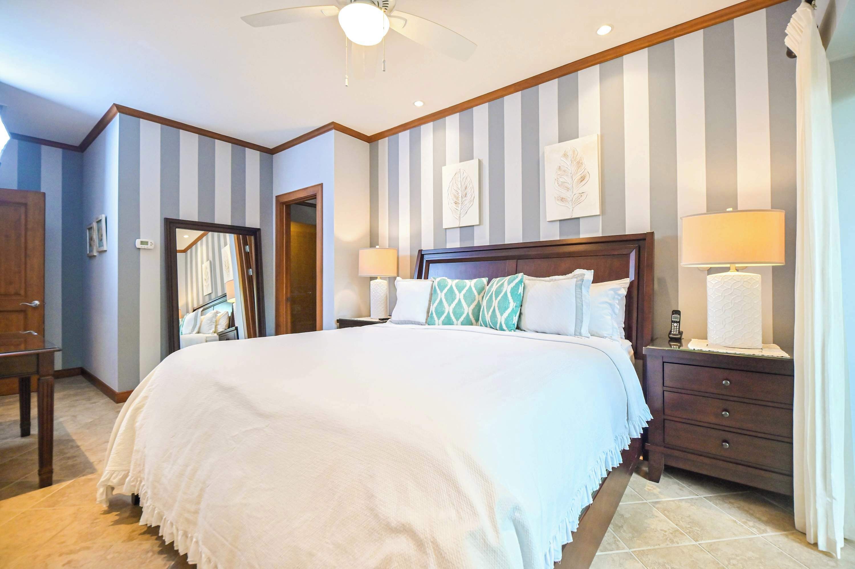 A hotel room with a large bed, two bedside tables with lamps, a ceiling fan, and striped walls.