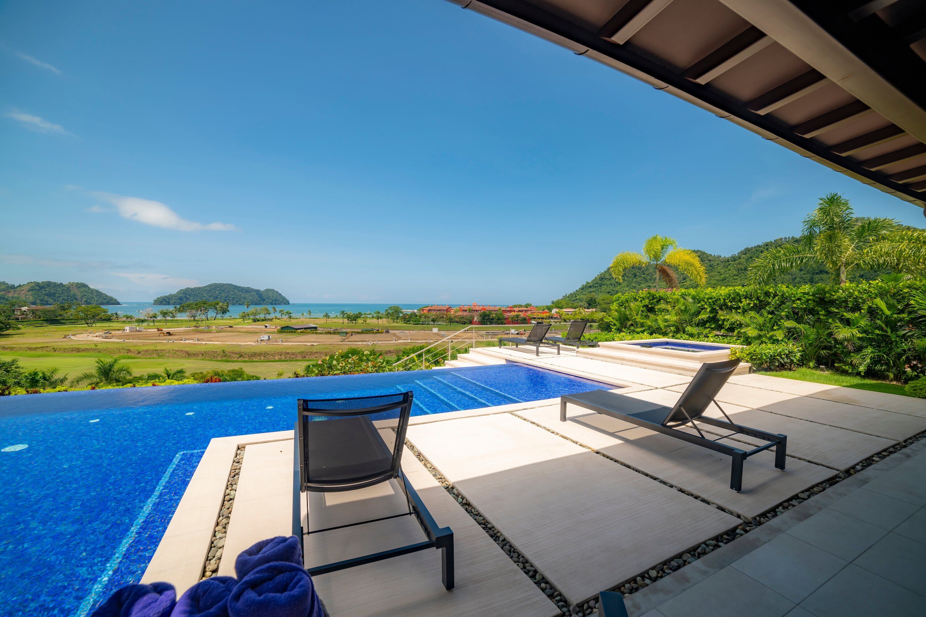 An infinity pool with lounge chairs and towels, overlooking a scenic landscape with hills and a distant view of the sea.