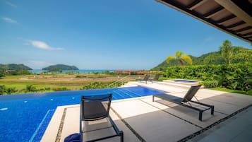 An infinity pool with lounge chairs and towels, overlooking a scenic landscape with hills and a distant view of the sea.