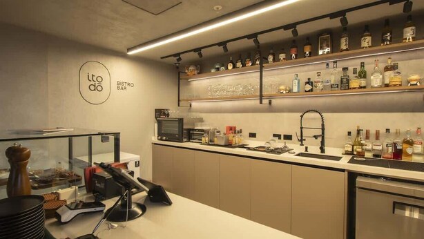 Eine moderne Bistro-Bar mit Küchenbereich, einer Glasvitrine und einer Auswahl an Flaschen auf Regalen.