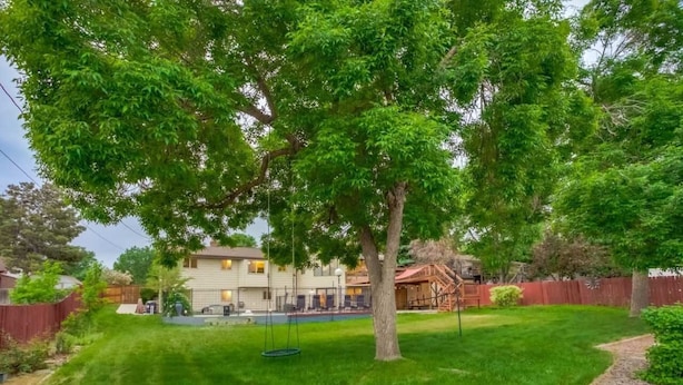 Un patio trasero con un columpio, una piscina y una casa con jardín cercado.