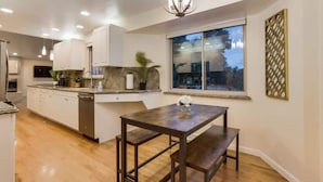 Una cocina moderna con armarios blancos, una mesa de comedor de madera y un ventanal grande.