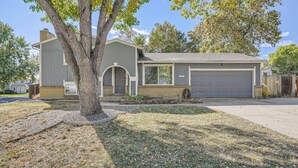 A single-story house with a garage, a tree in the front yard, and a clear sky. - Charming I Family Friendly I 4bd 2ba Arvada Home (Arvada)