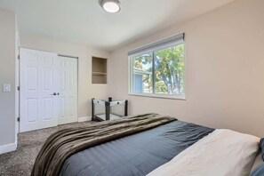 Quarto com cama, janela, porta e um pequeno armário.