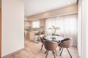 A modern kitchen with a microwave, a dining area with a round table and chairs, and a large window with curtains. - Piantini Gem Modern Apartment with Amenities (Santo Domingo)