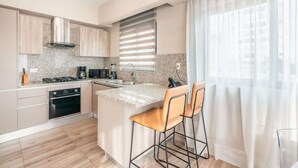 A modern kitchen with granite countertops, stainless steel appliances, and a large window with blinds. - Stylish Apartment in Piantini Pool & Gym u302 (Santo Domingo)