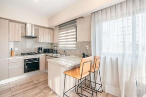 Eine moderne Küche mit Granit Arbeitsplatten, Edelstahlgeräten und einem gro ßen Fenster mit Jalousien.