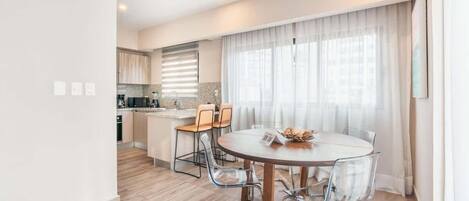 A modern kitchen with wooden cabinets, a dining area with a round table and chairs, and a large window with curtains.