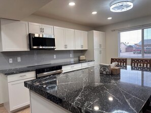 A modern kitchen with white cabinets, a black countertop, and a built-in microwave. - 3-bedroom house-Sloan park -with cool AC -ping pong table (Mesa)