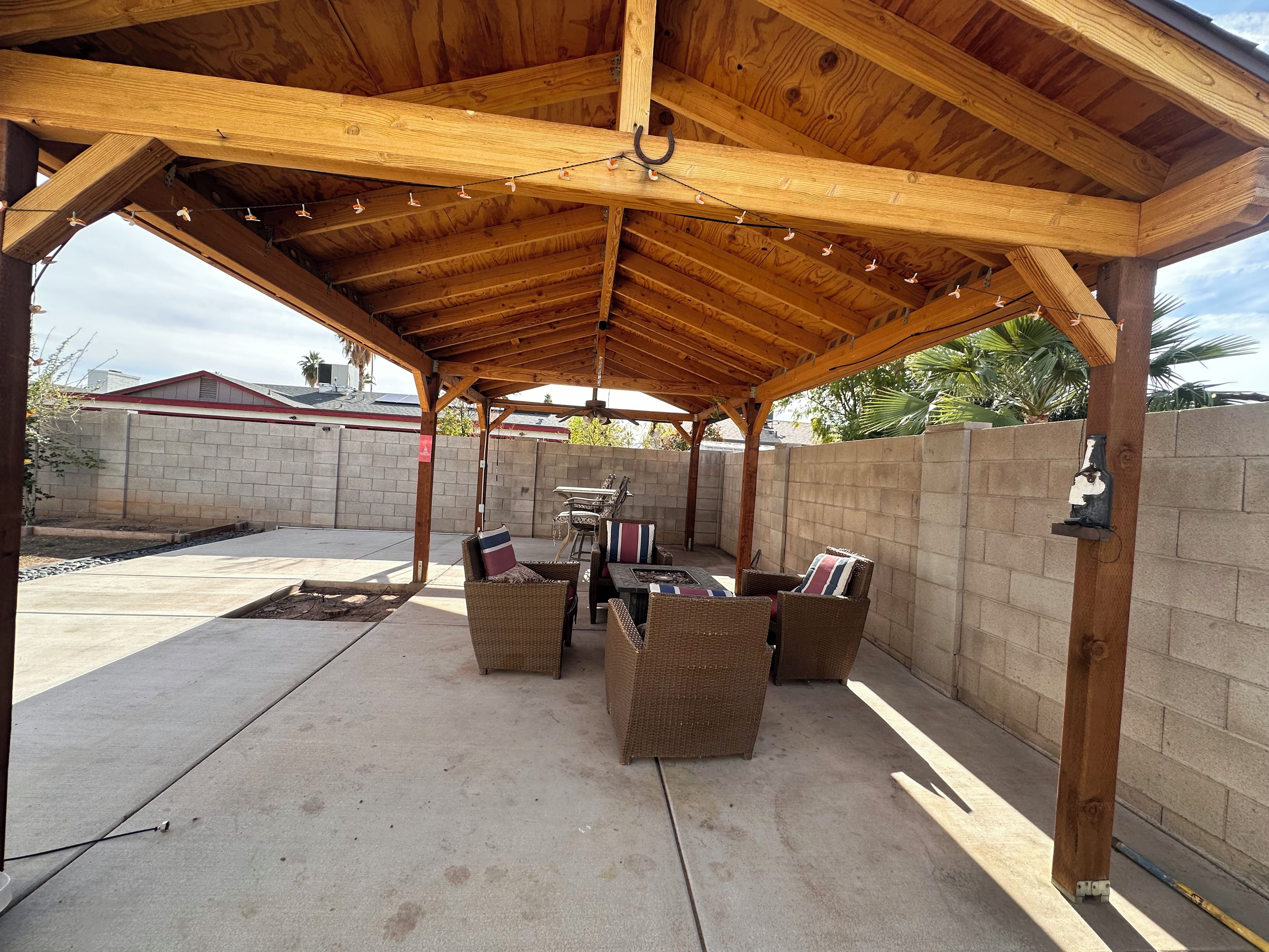 Ein überdachter Patio-Bereich mit Holzbalken, Korbmöbeln und einem Betonboden.
