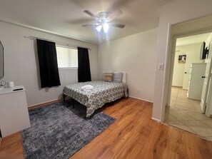 A bedroom with a bed, a ceiling fan, a window with curtains, a bedside table, and a door leading to another room. - 3-bedroom house-Sloan park -with cool AC -ping pong table (Mesa)