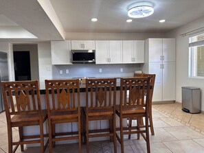 A kitchen with white cabinets, a microwave, and a dining area with wooden chairs. - 3-bedroom house-Sloan park -with cool AC -ping pong table (Mesa)