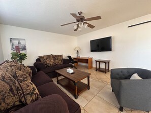 Ein Wohnzimmer mit Sofa, Sesseln, Couchtisch und Deckenventilator.