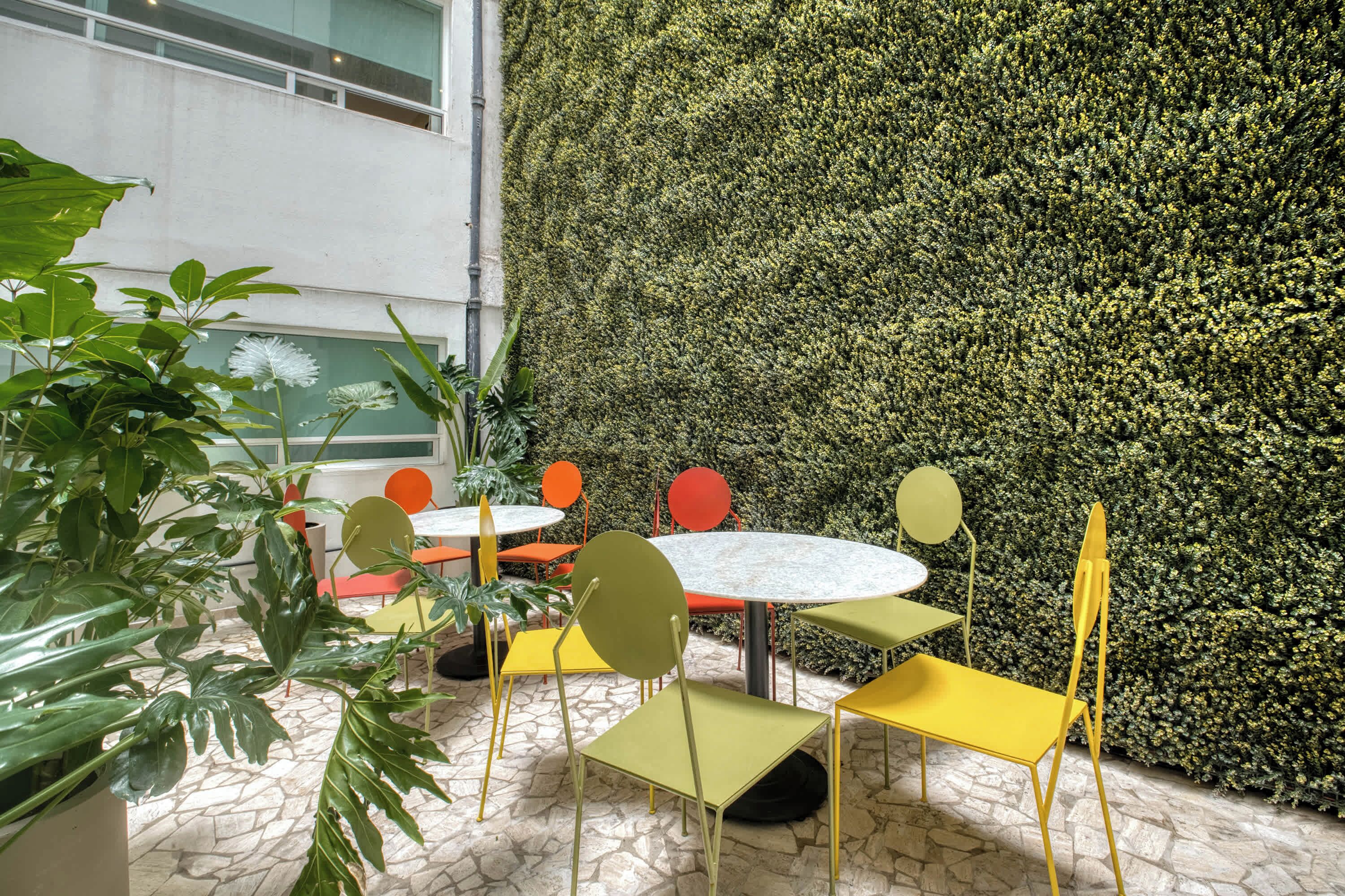 A dining area with round tables and chairs, a green wall with dense foliage, and potted plants.