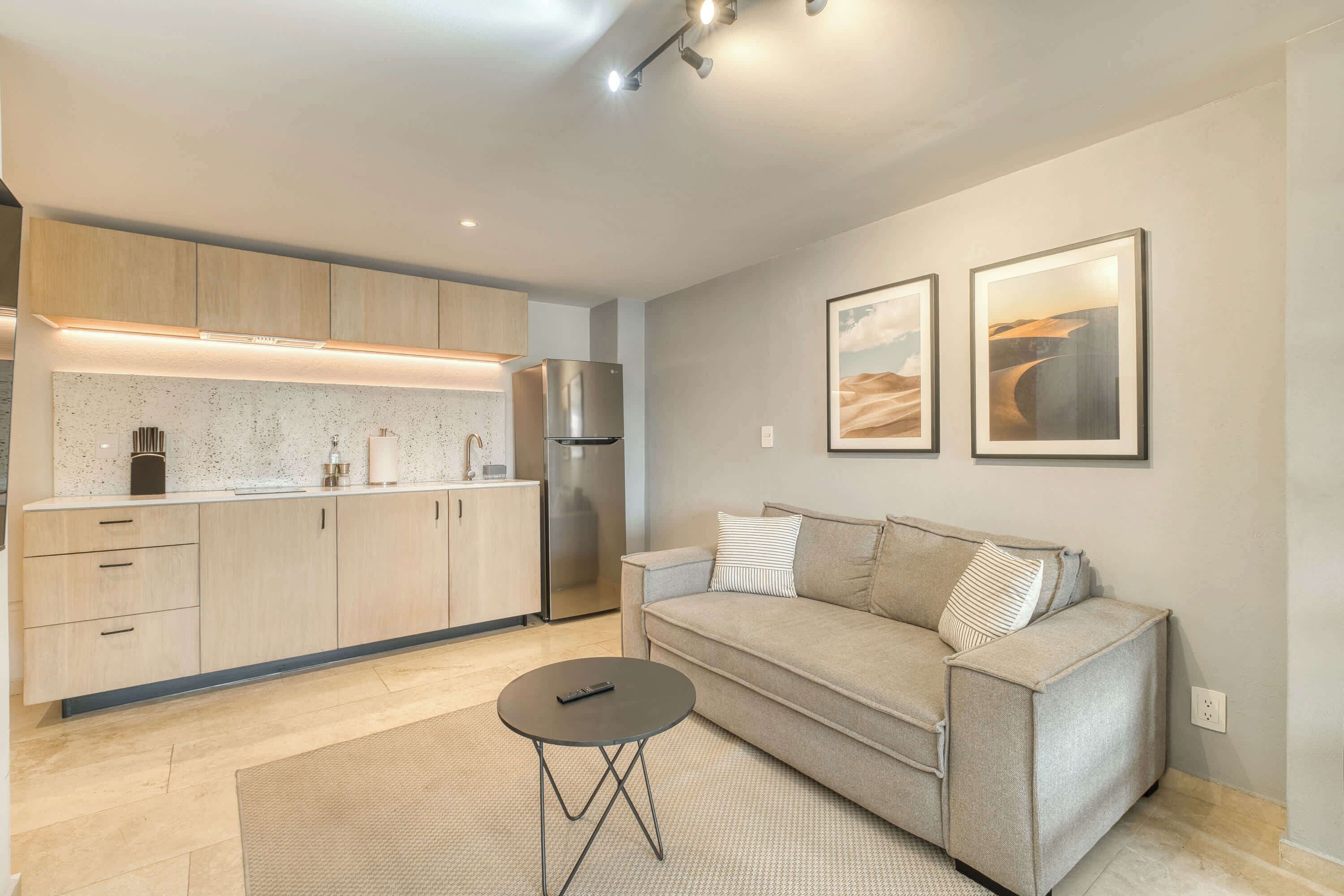 A modern living room with a sofa, a coffee table, and a kitchen area with cabinets and appliances.