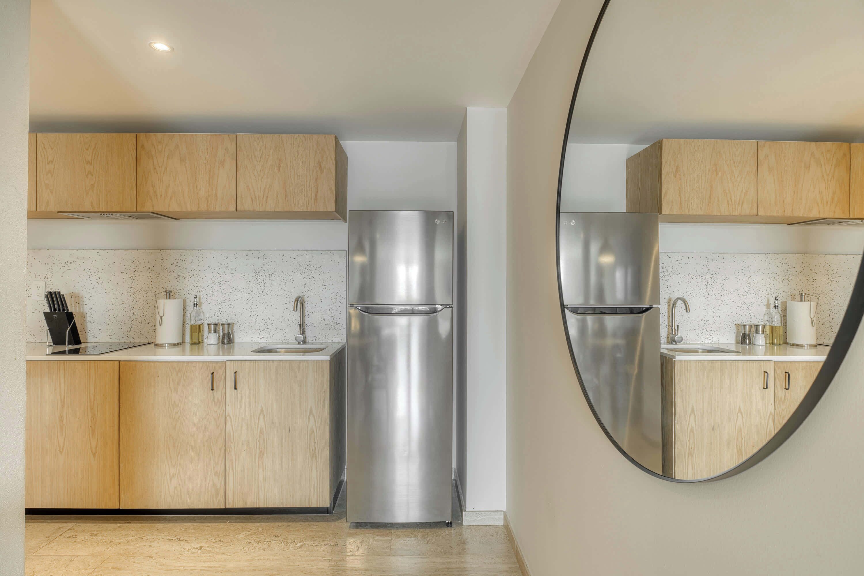 A modern kitchen with wooden cabinets, stainless steel appliances, and a round mirror.