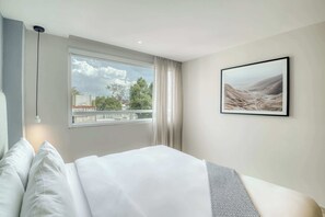 A hotel room with a large bed, a window with curtains, a hanging light, and a framed picture on the wall. - Modern King Studio in Central Roma Norte (Ciudad de México)