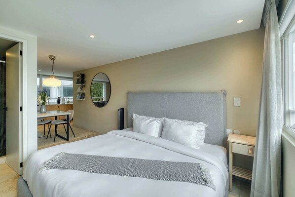 Une chambre d’hôtel moderne, dotée d’un grand lit, d’une table de chevet, d’un bureau et offrant une vue sur l’extérieur.
