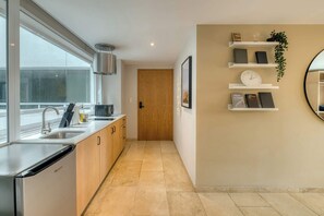 Eine moderne Küche mit Geschirrspüler, doppelter Spüle und Holzschränken. Es gibt einen Flur mit einer Holztür und einem an der Wand befestigten Regal mit Büchern und einer Uhr.
