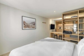 Ein modernes Hotelzimmer mit Bett, Schreibtisch, Fernseher und einer integrierten Küchenzeile.