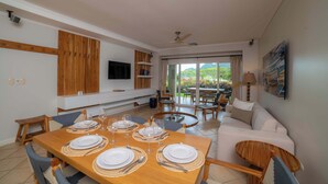 A dining area with a wooden table set for four, a sofa, and a TV mounted on the wall. - Del Mar 4N - 3 bdr 2 bath Family (Playa Herradura)