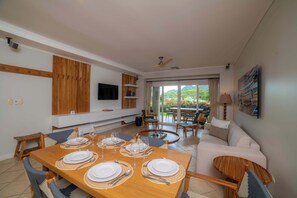 A dining area with a wooden table set for four, a sofa, and a TV mounted on the wall. - Del Mar 4N - 3 bdr 2 bath Family (Playa Herradura)