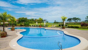 A swimming pool with a curved design, surrounded by lounge chairs and potted plants. - Del Mar 4N - 3 bdr 2 bath Family (Playa Herradura)