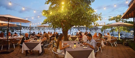 Un espace extérieur aménagé pour les repas, avec des tables, des chaises, des guirlandes lumineuses et des parasols.