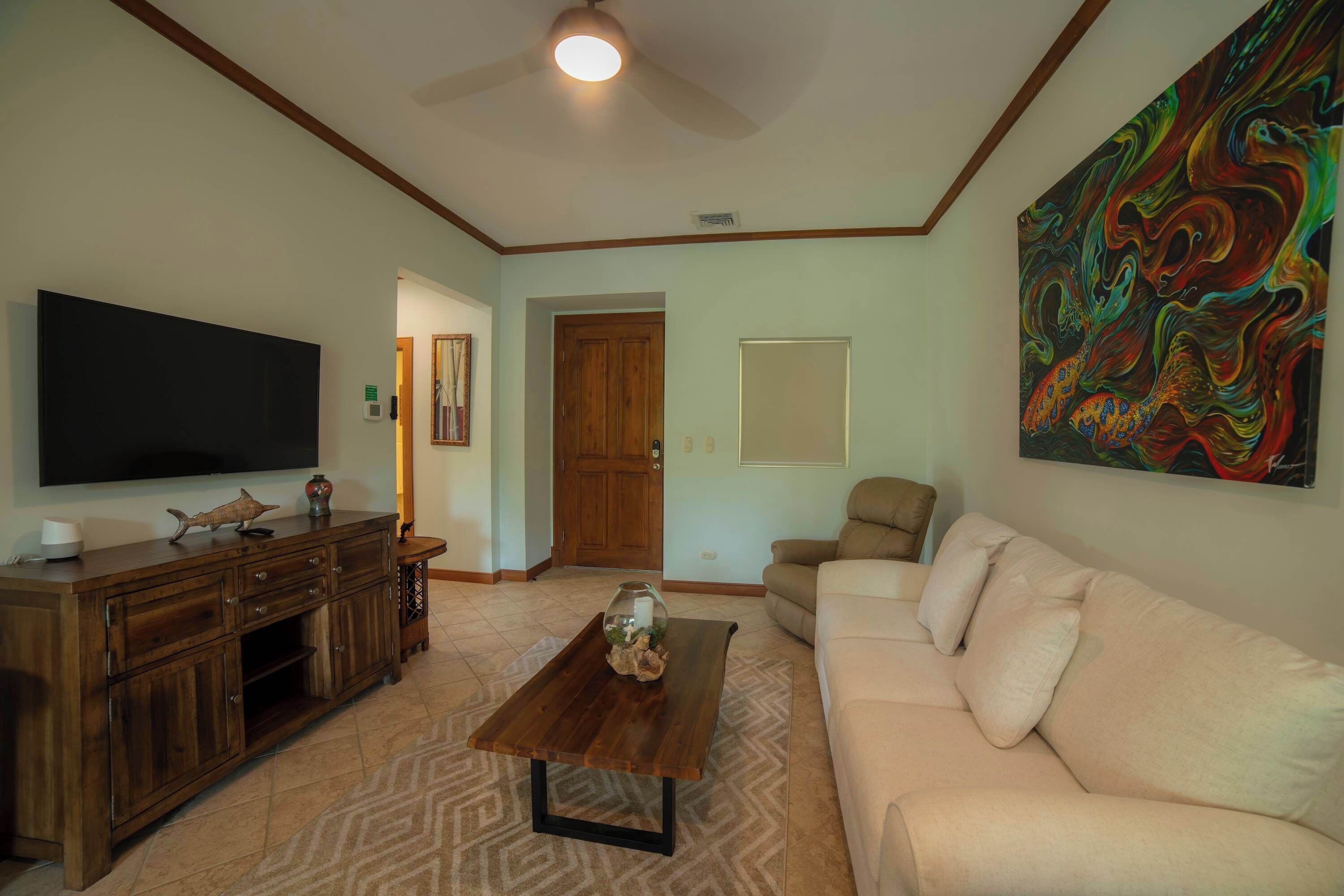 A living room with a TV, wooden entertainment center, beige sofa, coffee table, and a colorful abstract painting.