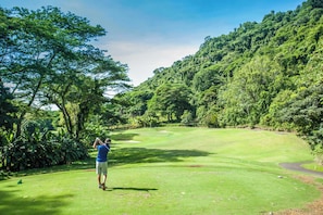 Un campo da golf con un paesaggio verdeggiante, alberi e cielo sereno.