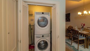 A laundry room with a front-loading washer and dryer, a dining area with a table and chairs, and a chandelier.