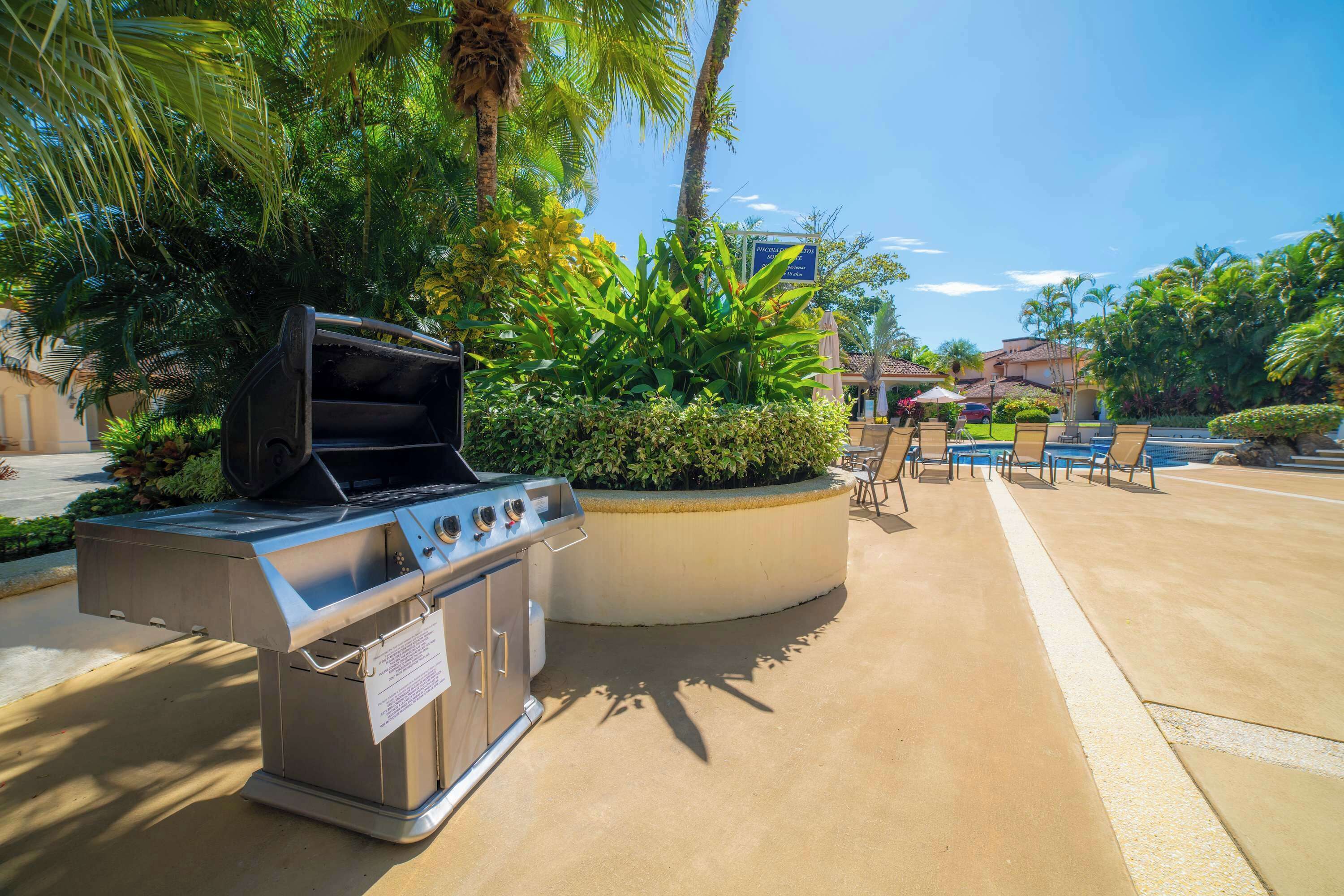 Un área de parrilla al aire libre con un conjunto de asientos junto a la piscina.