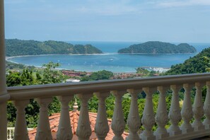 A balcony with a view of a coastal landscape, including a bay with boats and a forested hill. - Casa Garmus - 10 bdr Ocean View (Playa Herradura)