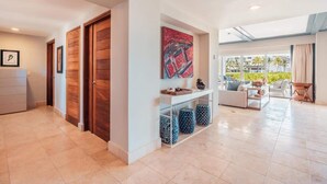 A spacious living area with a sofa set, a coffee table, and a console table with decorative items. There is a large window providing a view of the outdoors. - Apt with 2br-beachfront private pool in Sotogrande (Punta Cana)