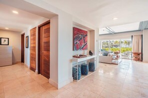 A spacious living area with a sofa set, a coffee table, and a console table with decorative items. There is a large window providing a view of the outdoors. - Apt with 2br-beachfront private pool in Sotogrande (Punta Cana)