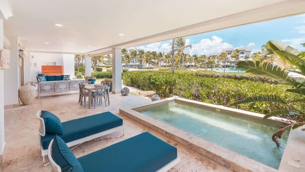 A modern outdoor lounge area with a pool, seating, and a view of a resort. - Apt with 2br-beachfront private pool in Sotogrande (Punta Cana)