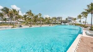 A large, clear swimming pool surrounded by palm trees and modern buildings. - Apt with 2br-beachfront private pool in Sotogrande (Punta Cana)