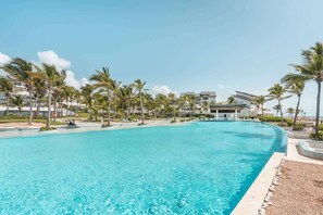 A large, clear swimming pool surrounded by palm trees and modern buildings. - Apt with 2br-beachfront private pool in Sotogrande (Punta Cana)